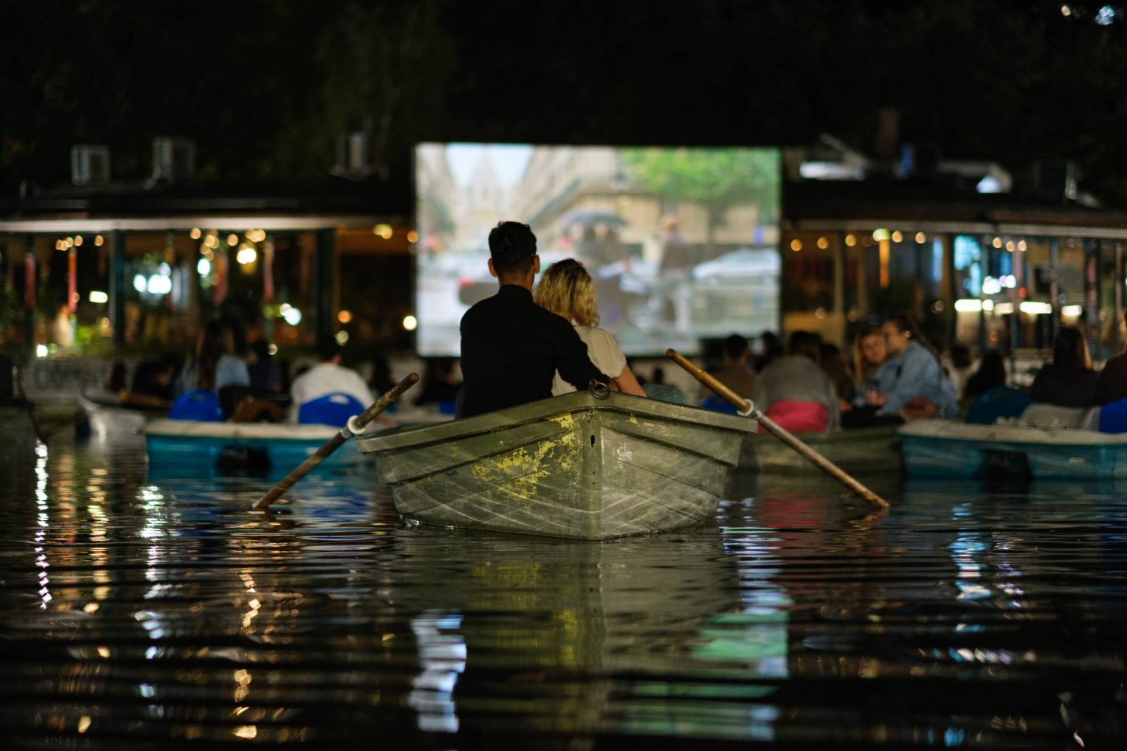 Two viewers in a boat on the lake, in front of the cinema screen.