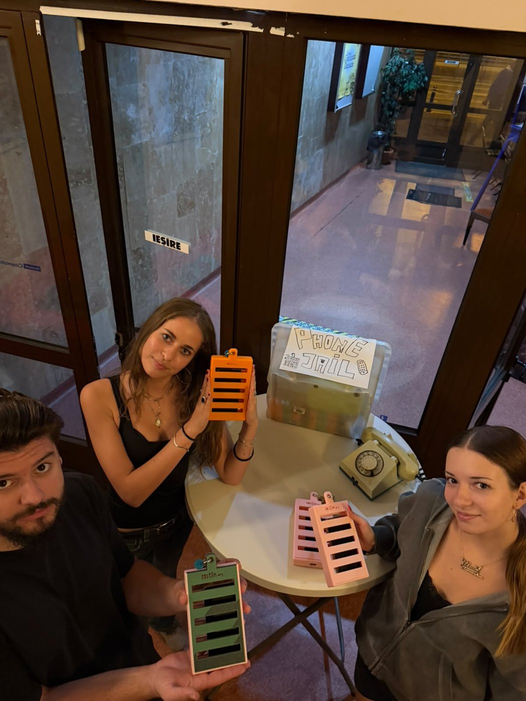 Trei membri ai echipei cu phone jail-uri colorate, în jurul mesei din foaier.