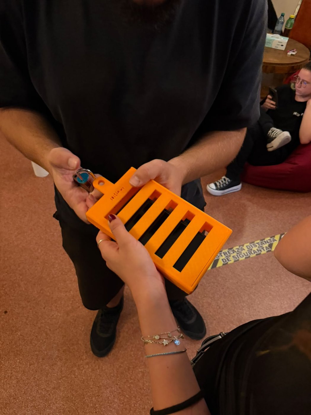 Un phone jail portocaliu printat 3D, cu lacăt și cheie, ținut în mâini.