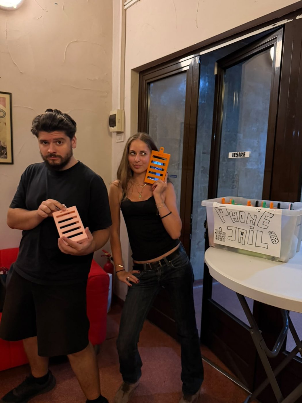 Doi voluntari țin phone jail-uri printate 3D, lângă cutia „Phone Jail” din foaierul Cinema Europa.